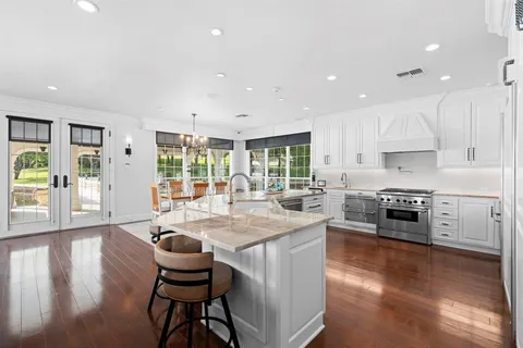 a kitchen with stainless steel appliances granite countertop a stove a sink a refrigerator white cabinets and wooden floor next to a window