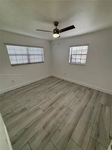 an empty room with wooden floor ceiling fan and windows