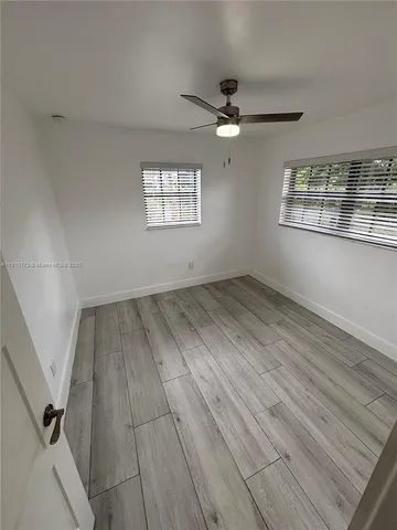 an empty room with wooden floor fan and windows