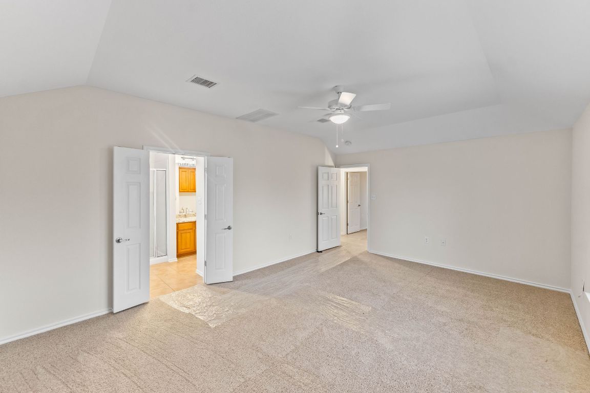 292 Housefinch Loop Leander, TX 78641 - Photo 15 of 29 Unfurnished bedroom featuring light colored carpet, vaulted ceiling, a ceiling fan, and connected bathroom