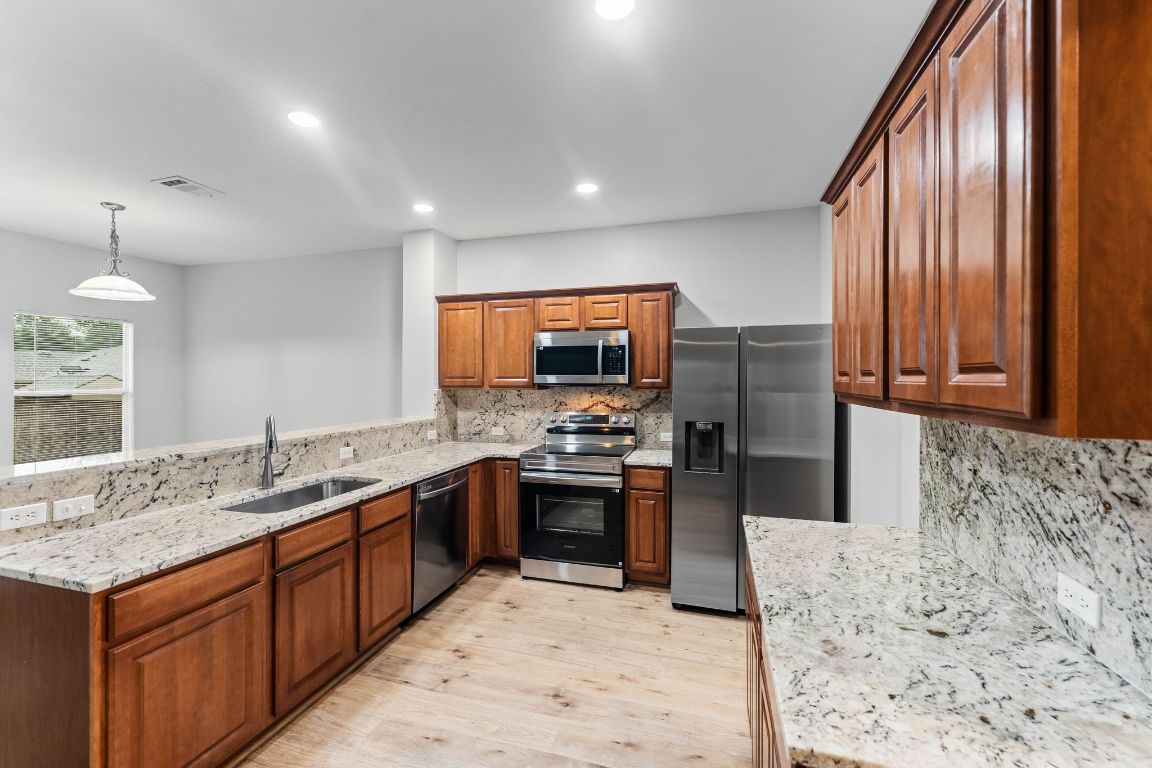 292 Housefinch Loop Leander, TX 78641 - Photo 4 of 29 Kitchen featuring stainless steel appliances, light wood-type flooring, backsplash, light stone countertops, and a peninsula