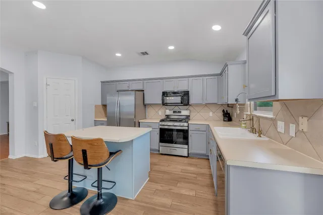 a kitchen with stainless steel appliances kitchen island a table chairs sink and cabinets