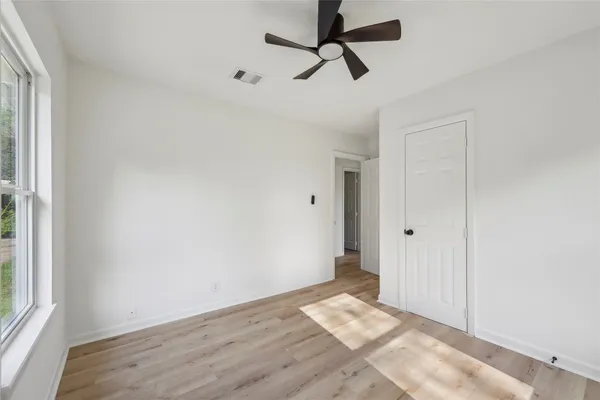 a view of empty room with wooden floor and fan