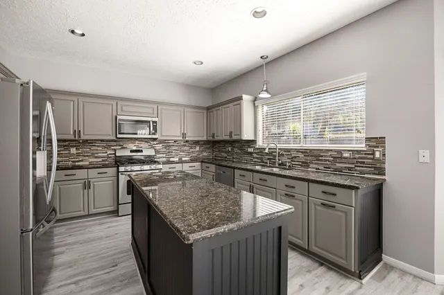 a kitchen with stainless steel appliances granite countertop a stove a sink dishwasher a refrigerator and a microwave oven with wooden floor