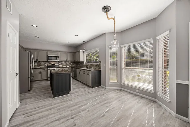 a kitchen with stainless steel appliances kitchen island granite countertop a refrigerator a sink dishwasher a stove and a dining table with wooden floor