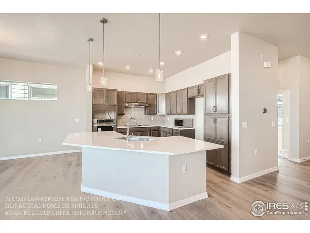 a large white kitchen with stainless steel appliances kitchen island a stove a refrigerator a oven and a sink with large countertops