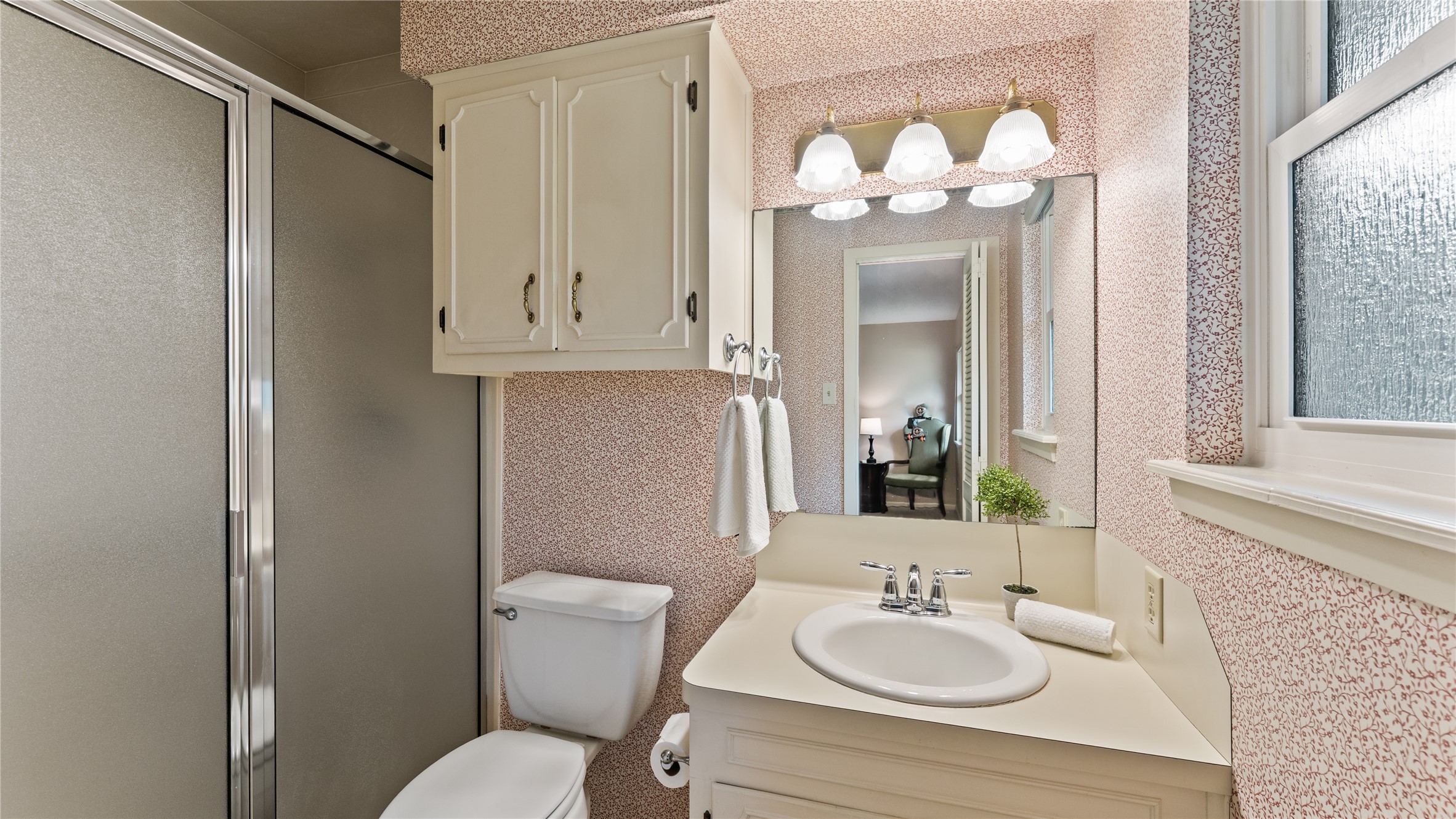 208 Magnolia Way Huntsville, TX 77320 - Photo 21 of 26 The primary bathroom features a design with a shower, cabinet for storage, and a vanity with a sink. The space is well-lit with a three-bulb fixture above the mirror, and there's a window for natural light.
