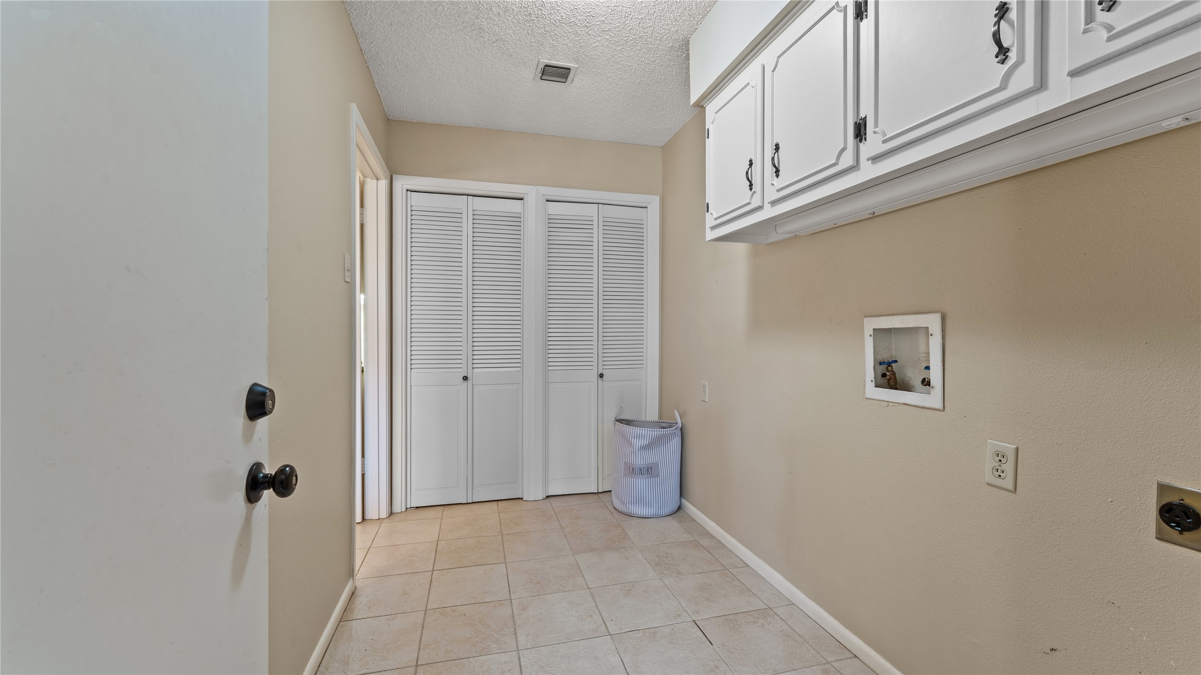 208 Magnolia Way Huntsville, TX 77320 - Photo 22 of 26 This photo shows a laundry room with tile flooring, neutral walls, and overhead white cabinets for storage. It features a utility hookup and a closet with louvered doors, providing additional storage space.