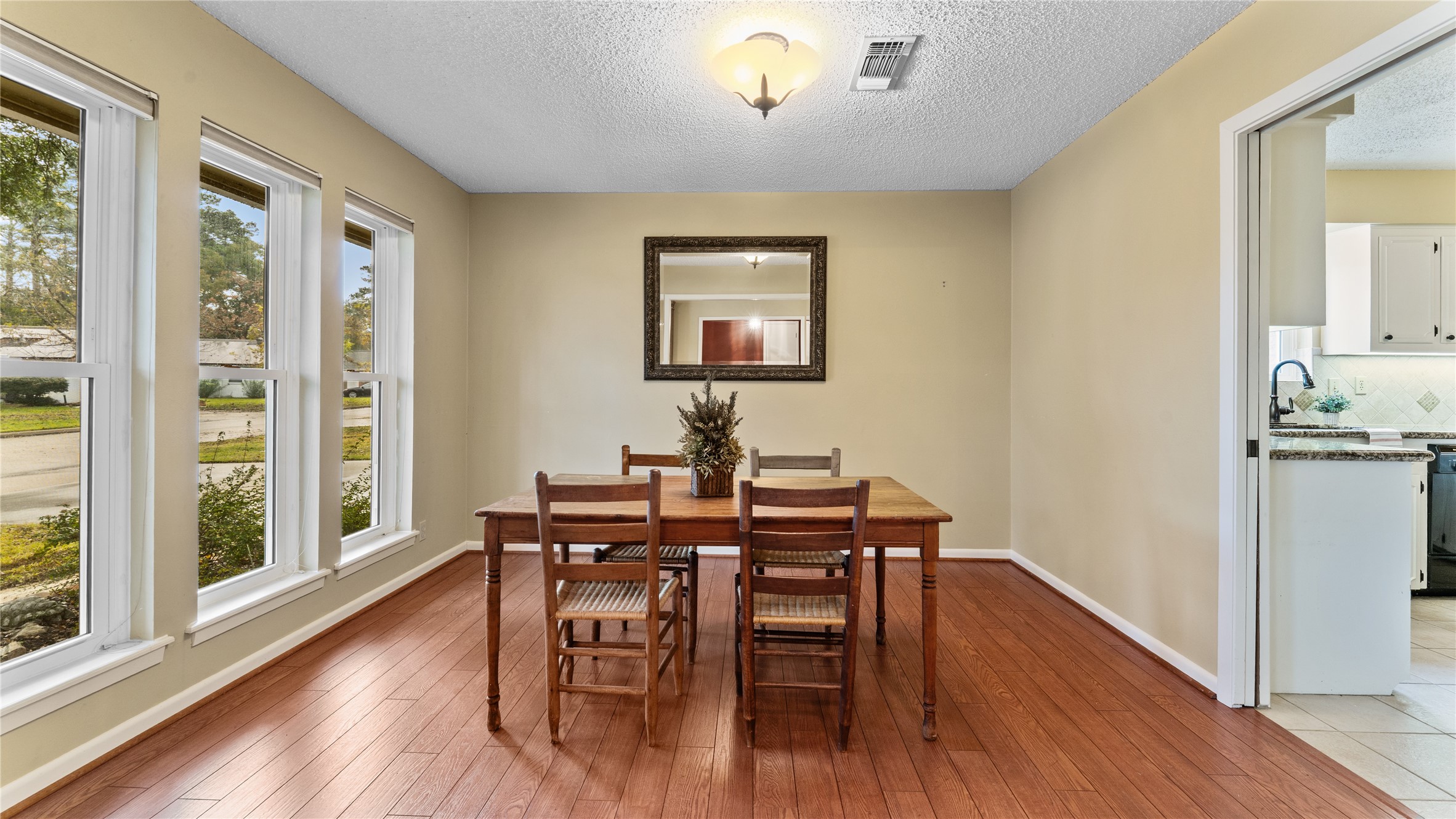 208 Magnolia Way Huntsville, TX 77320 - Photo 8 of 26 Bright dining area with hardwood floors, featuring a dining table and chairs. Large windows bring in natural light, and there's easy access to the adjacent kitchen. Neutral walls and a dimmable ceiling light add warmth.