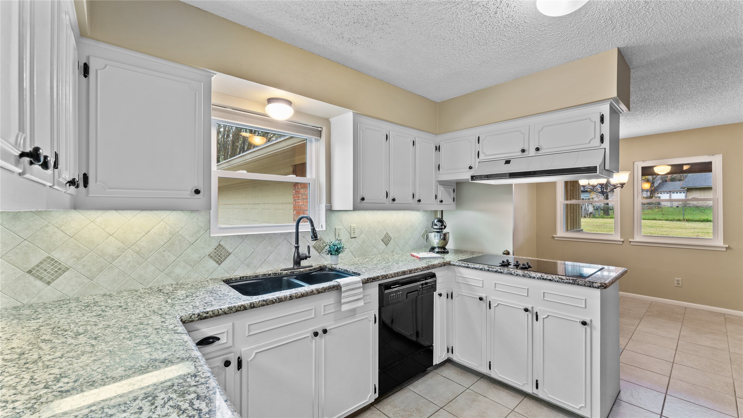 208 Magnolia Way Huntsville, TX 77320 - Photo 9 of 26 This kitchen features white cabinetry, granite countertops, and an updated tile backsplash. It includes a large double sink, newer sink fixture, electric cooktop, 2-built-in stoves, and dishwasher. Natural light comes in through a window over the sink, and there's an open view to the adjacent dining area with tiled flooring. (Fridge is excluded from sale).