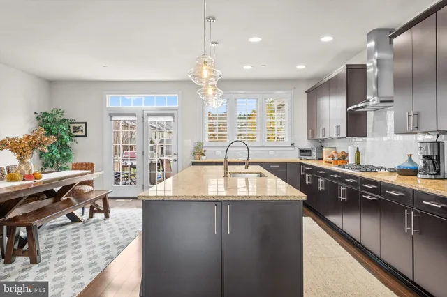 a kitchen with stainless steel appliances granite countertop a sink dishwasher a refrigerator and a dining table with wooden floor