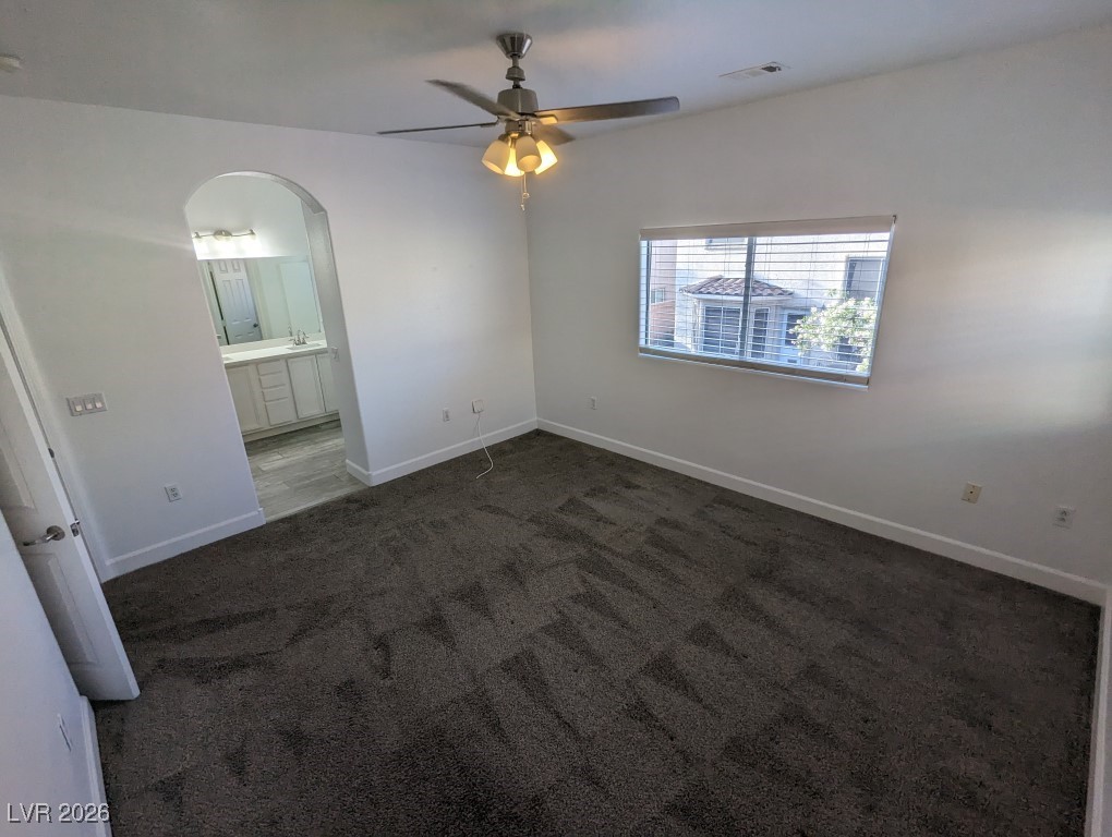 9303 Gilcrease Avenue, Unit 1137 Las Vegas, NV 89149 - Photo 19 of 30 Unfurnished bedroom with a ceiling fan, arched walkways, dark colored carpet, and ensuite bathroom