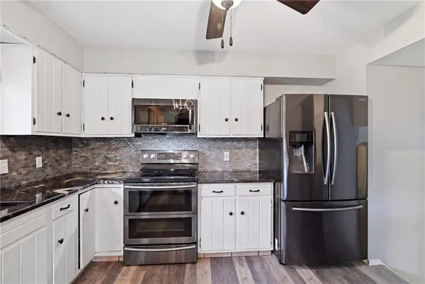 a kitchen with stainless steel appliances granite countertop a refrigerator a sink dishwasher a stove top oven a refrigerator with white cabinets and wooden floor