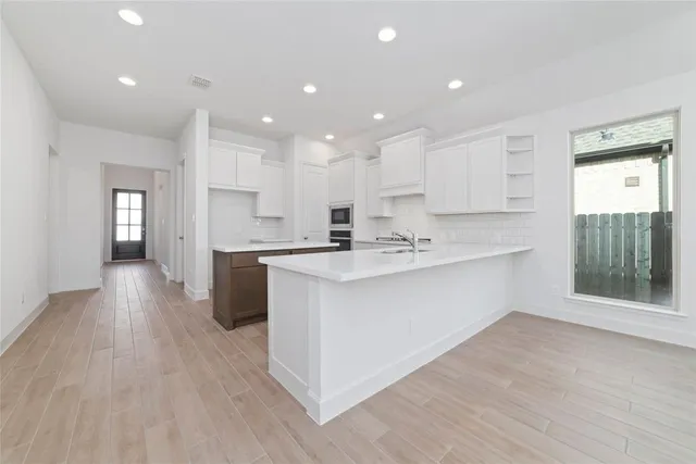 a large white kitchen with kitchen island a sink wooden floor and a refrigerator