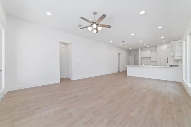 a view of an empty room with a ceiling fan and kitchen view