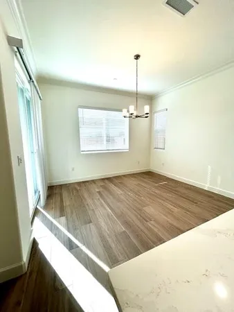 an empty room with wooden floor chandelier and windows