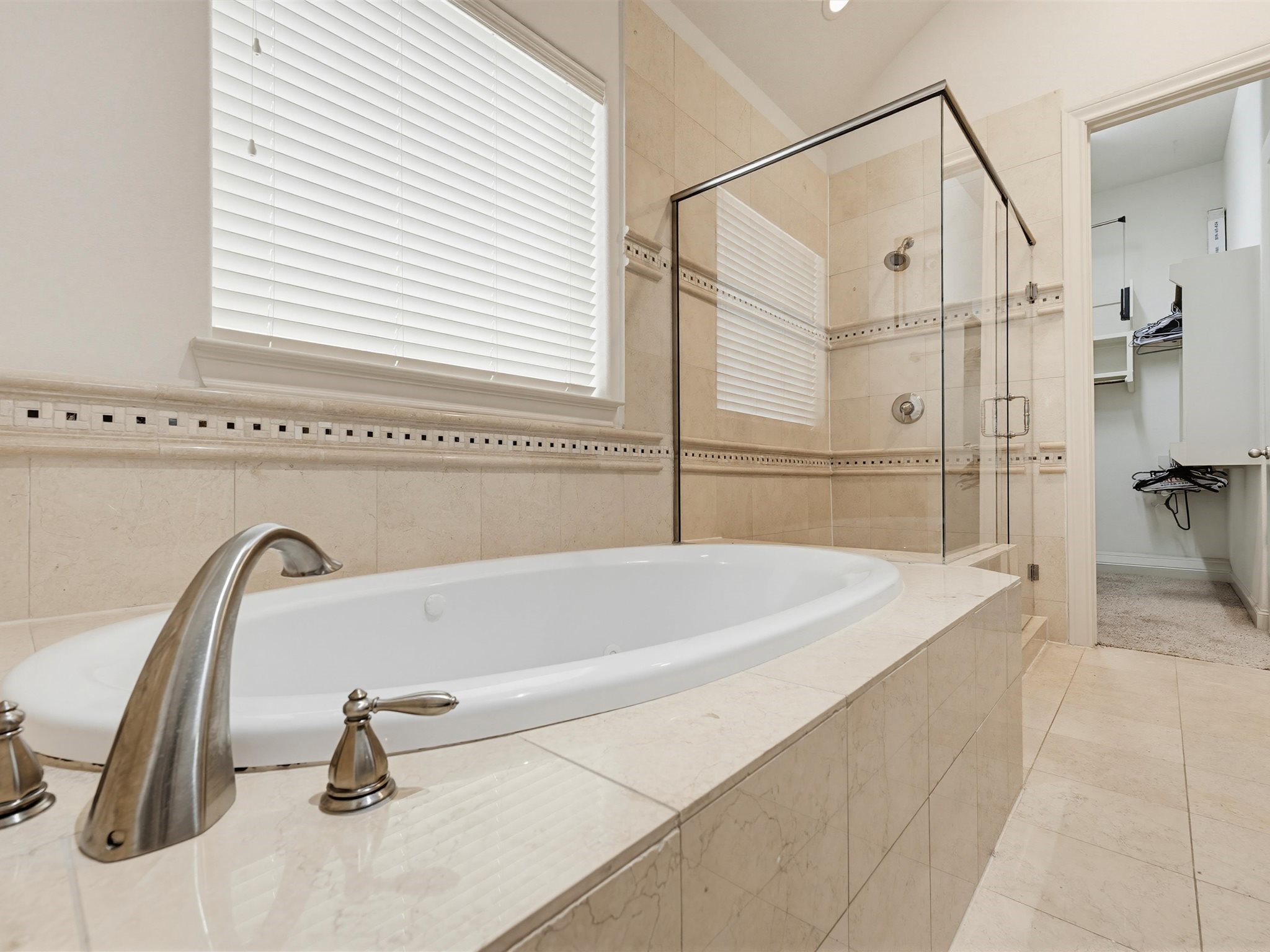 9427 London Bridge Station Houston, TX 77045 - Photo 25 of 30 This bathroom features a luxurious soaking tub with elegant fixtures, adjacent to a spacious glass-enclosed shower. The neutral tile and ample natural light create a serene, spa-like atmosphere.