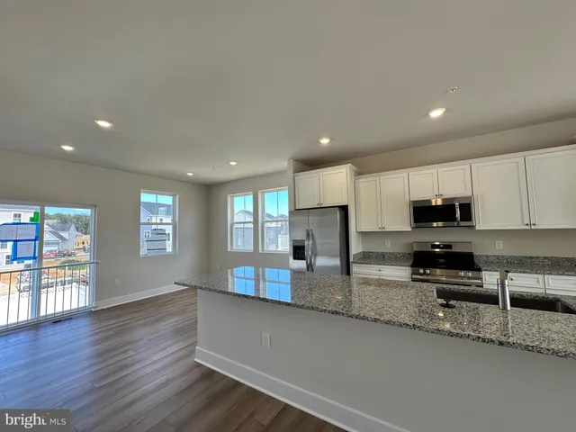 a kitchen with stainless steel appliances granite countertop a sink a stove a refrigerator a microwave a sink and white cabinets with wooden floor