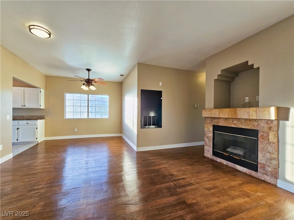 1851 Hillpointe Road, Unit 2124 Henderson, NV 89074 - Photo 6 of 24 Unfurnished living room featuring a tiled fireplace, baseboards, ceiling fan, and dark wood-type flooring