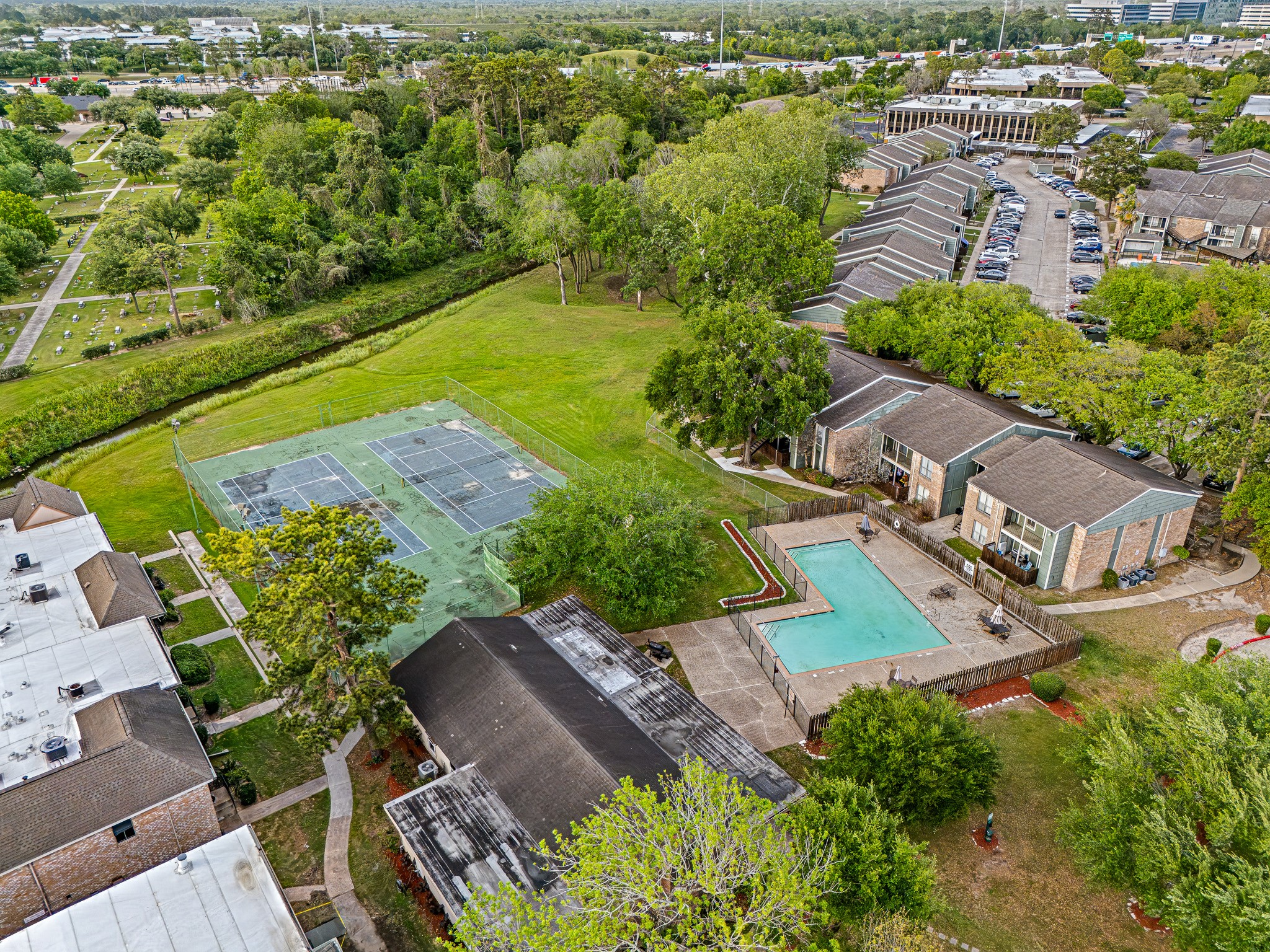 830 Threadneedle Street, Unit 240 Houston, TX 77079 - Photo 32 of 33 This aerial view showcases a residential complex with a swimming pool, tennis courts, and abundant green space. The surrounding area includes well-maintained buildings and easy access to nearby amenities, offering a blend of leisure and convenience.