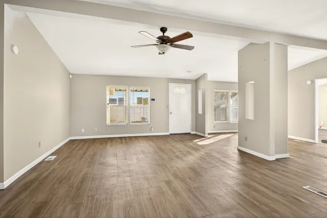 a view of an empty room with wooden floor and a ceiling fan