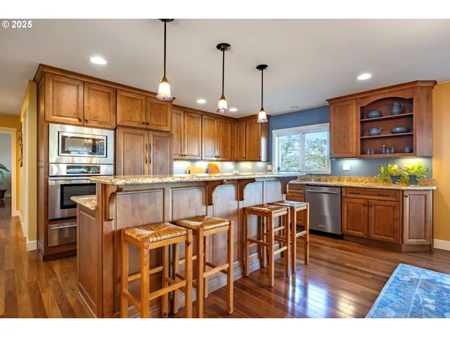 a kitchen with stainless steel appliances granite countertop a refrigerator a sink dishwasher a dining table and chairs with wooden floor