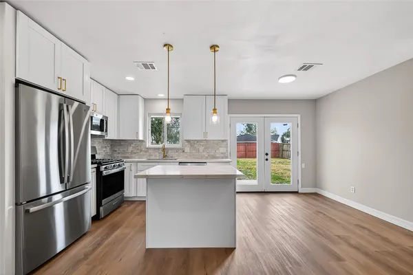 a kitchen with stainless steel appliances granite countertop a refrigerator a sink dishwasher a stove and a large refrigerator with wooden floor
