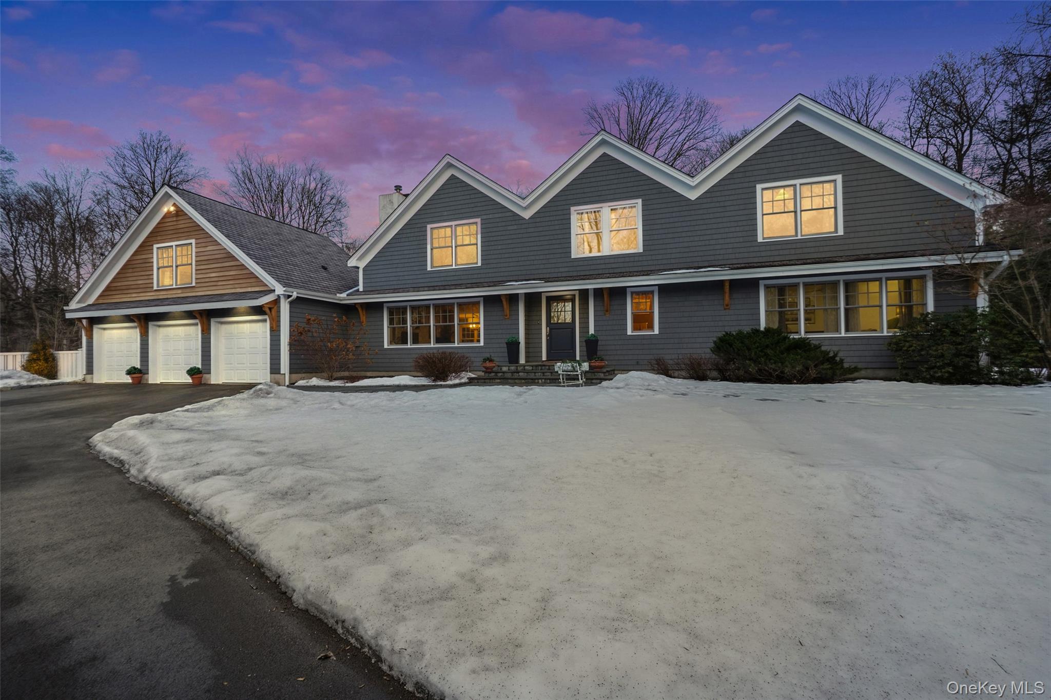 Twilight view of front of property with a three car garage,  covered porch and a two-toned cedar exterior.