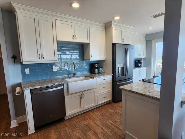 a kitchen with stainless steel appliances granite countertop a refrigerator a sink dishwasher a stove and white countertops with wooden floor