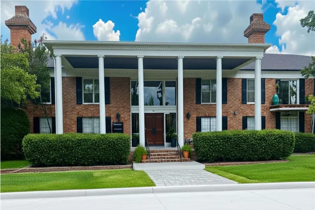 a view of a brick house with a yard plants and a large tree
