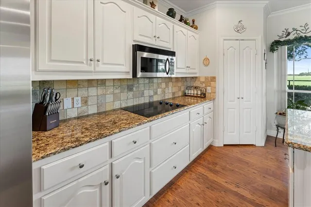 a large kitchen with stainless steel appliances granite countertop a sink dishwasher stove and white cabinets with wooden floor