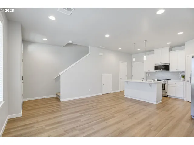 a view of kitchen with kitchen island granite countertop stainless steel appliances refrigerator oven stove and white cabinets with wooden floor