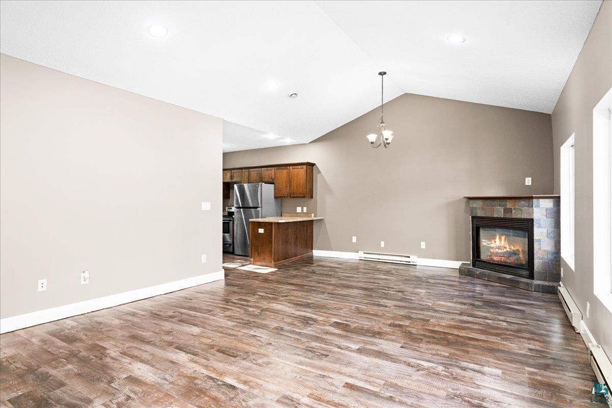 3757 Haines Road Hermantown, MN 55811 - Photo 4 of 22 Unfurnished living room featuring a tile fireplace, a baseboard heating unit, lofted ceiling, and hardwood / wood-style floors