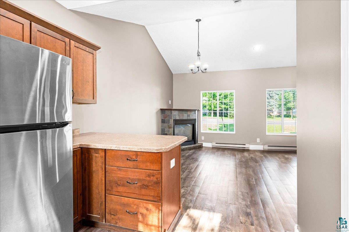 3757 Haines Road Hermantown, MN 55811 - Photo 8 of 22 Kitchen with stainless steel fridge, a fireplace, a baseboard heating unit, lofted ceiling, and dark hardwood / wood-style flooring
