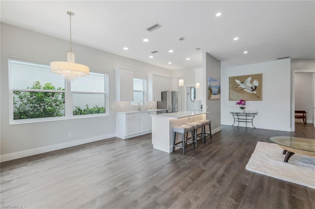 4648 Rio Poco Court Naples, FL 34109 - Photo 11 of 27 Kitchen with freestanding refrigerator, light countertops, a kitchen bar, white cabinetry, and wood finished floors