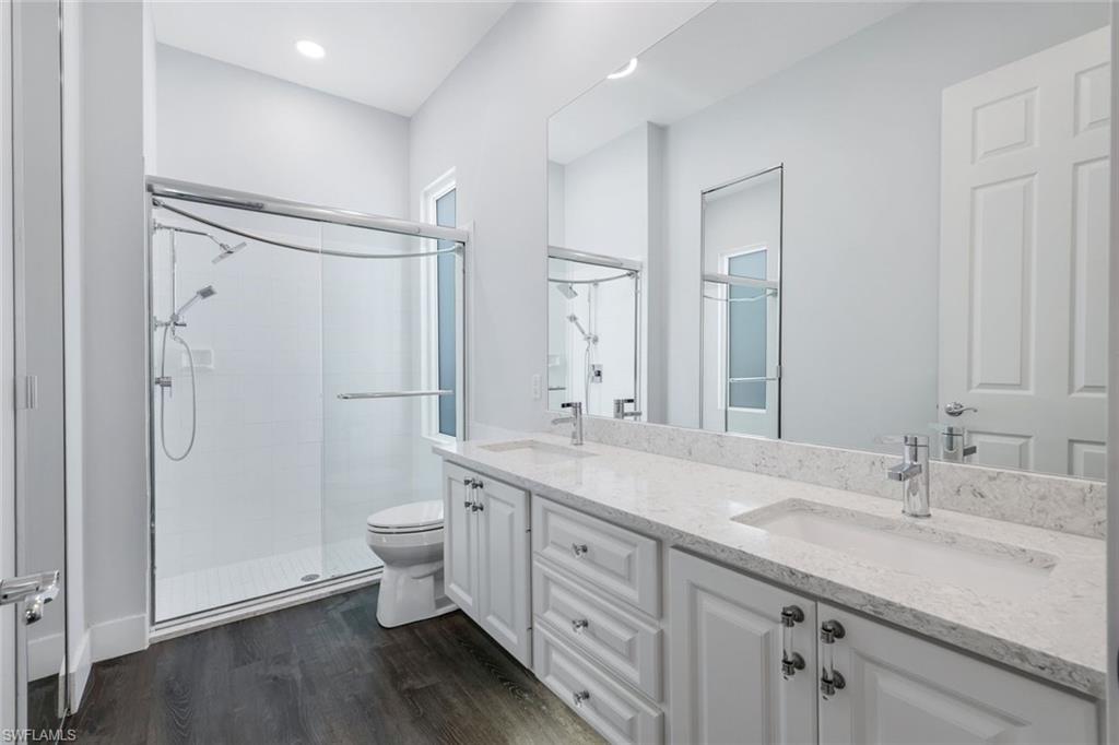 4648 Rio Poco Court Naples, FL 34109 - Photo 20 of 27 Master Bathroom with double vanity, a shower stall, toilet, and recessed lighting. Note: Dated glass bricks in shower have been replaced with beautiful Impact Glass.