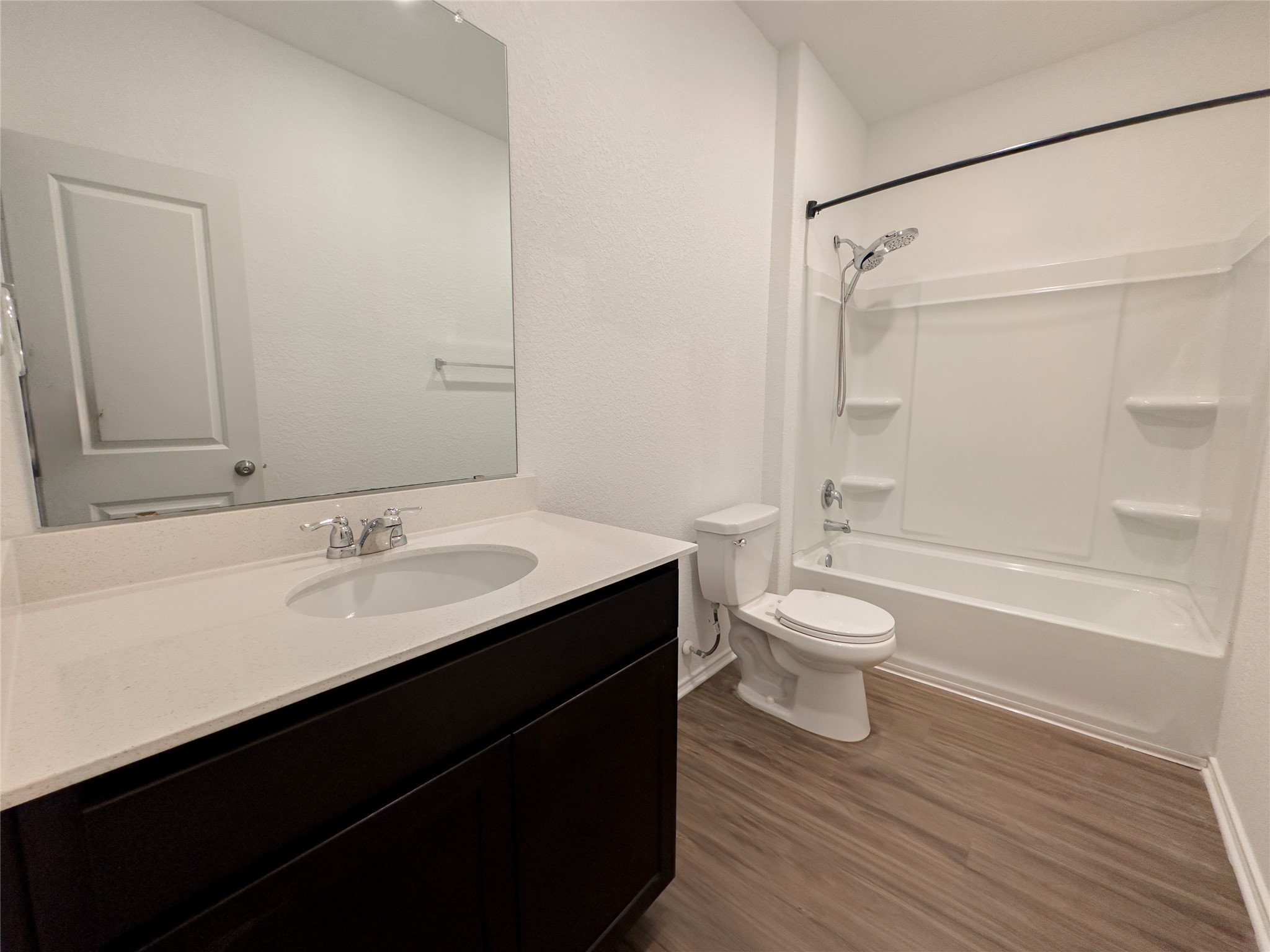 312 Soapstone Pass Maxwell, TX 78656 - Photo 15 of 21 Full bathroom featuring a dark wood-finish vanity with an integrated sink and light-toned countertop, a frameless wall mirror, a white toilet, and a combination tub/shower with a white surround and a dark-finish shower rod