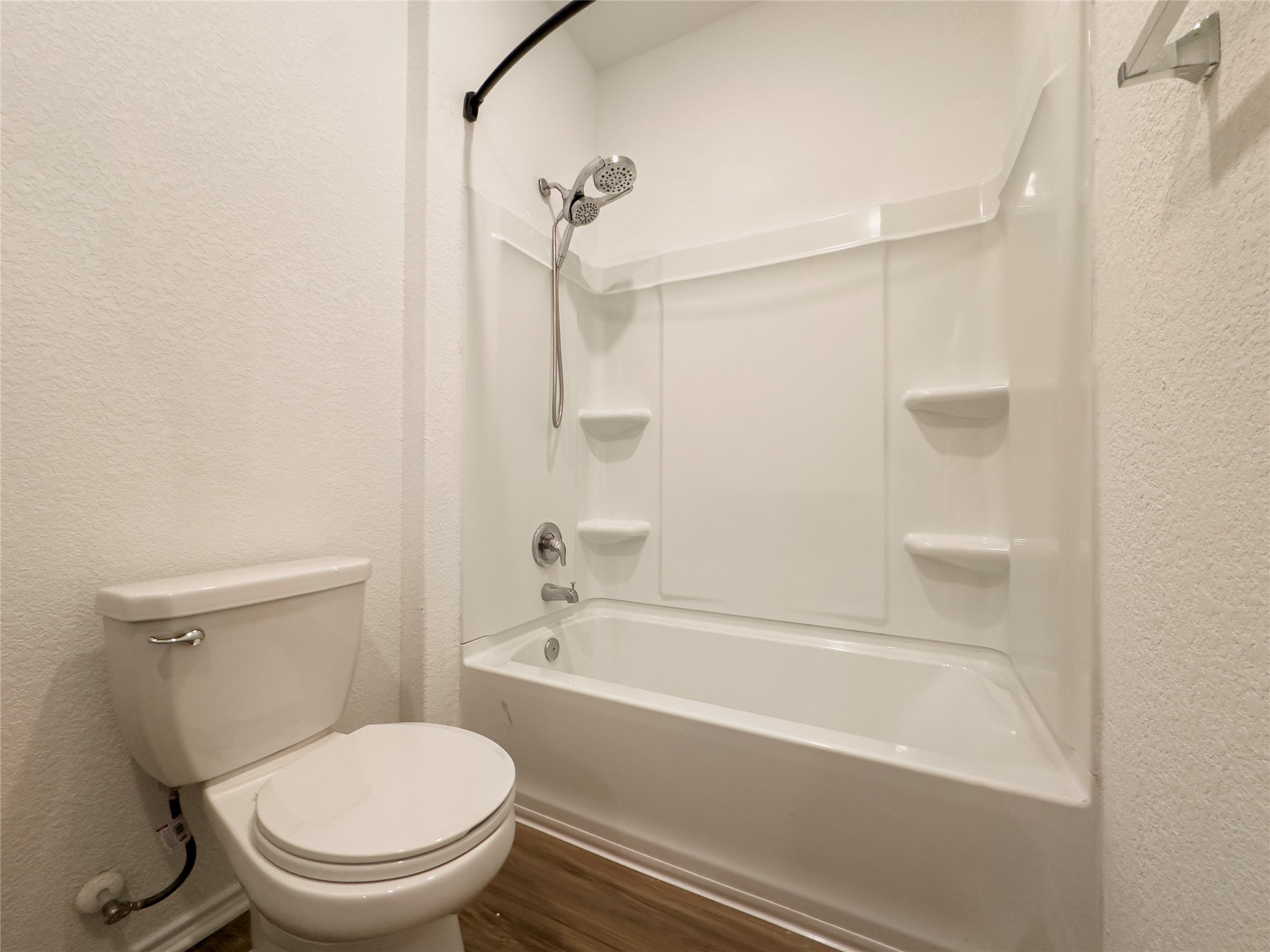 312 Soapstone Pass Maxwell, TX 78656 - Photo 16 of 21 Bathroom featuring a white tub and shower combination with an integrated shower caddy, a curved shower curtain rod, a chrome showerhead with a handheld sprayer, wood-finish flooring, and a white toilet with a chrome flush lever