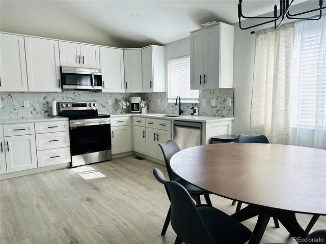 a kitchen with stainless steel appliances granite countertop a stove a sink dishwasher white refrigerator a dining table and chairs with wooden floor