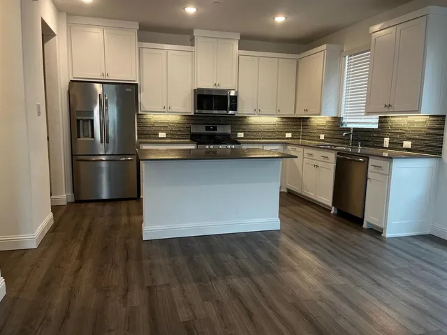 a kitchen with stainless steel appliances granite countertop a refrigerator stove a sink and a granite counter tops with wooden floors