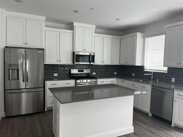 a kitchen with stainless steel appliances granite countertop a refrigerator a sink a stove a microwave and wooden floors