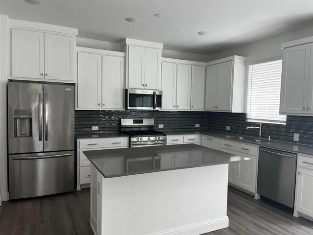 a kitchen with stainless steel appliances granite countertop a refrigerator a sink a stove a microwave and wooden floors