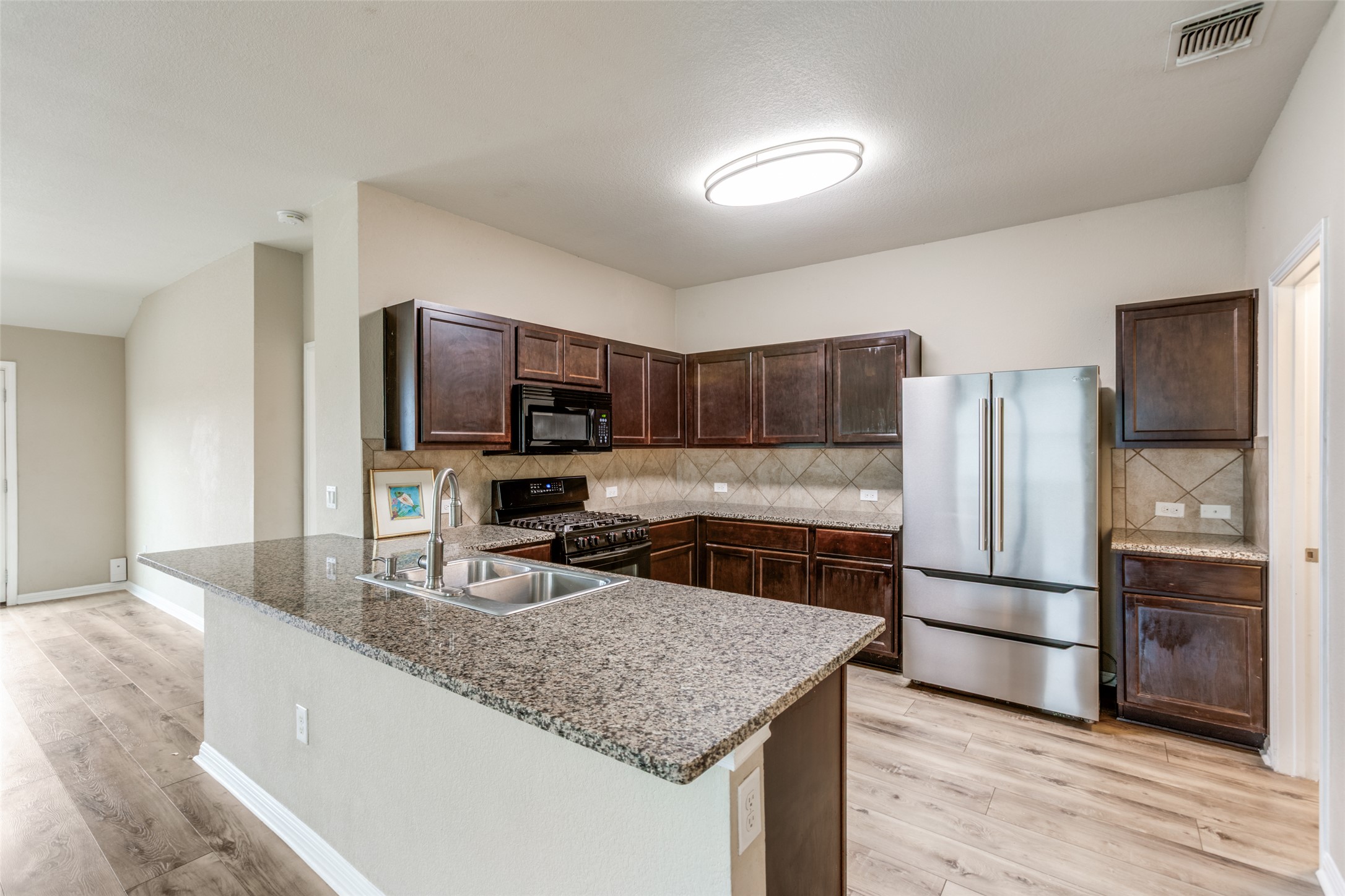 2909 Centrum Drive Austin, TX 78754 - Photo 15 of 30 The kitchen features an island with a double sink, dark wood cabinetry, stainless steel appliances, and light-colored flooring