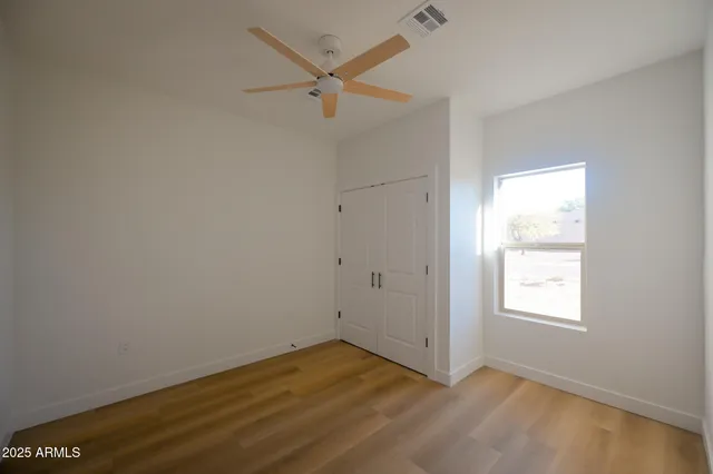 an empty room with wooden floor closet and windows