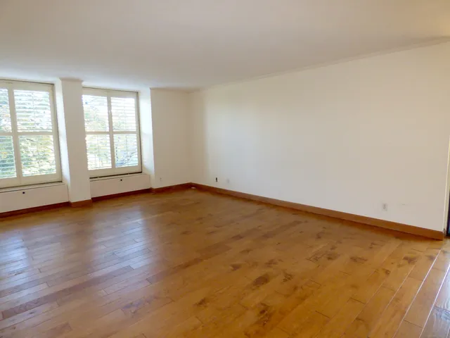 an empty room with wooden floor and windows with curtains