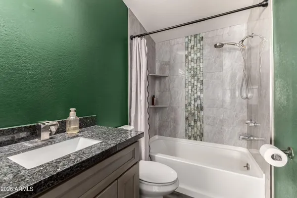 a bathroom with a granite countertop bathtub shower sink vanity and toilet