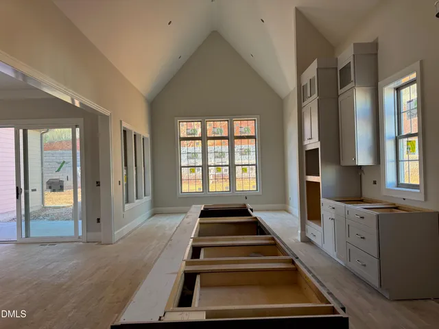 a view of an empty room with wooden floor and a kitchen