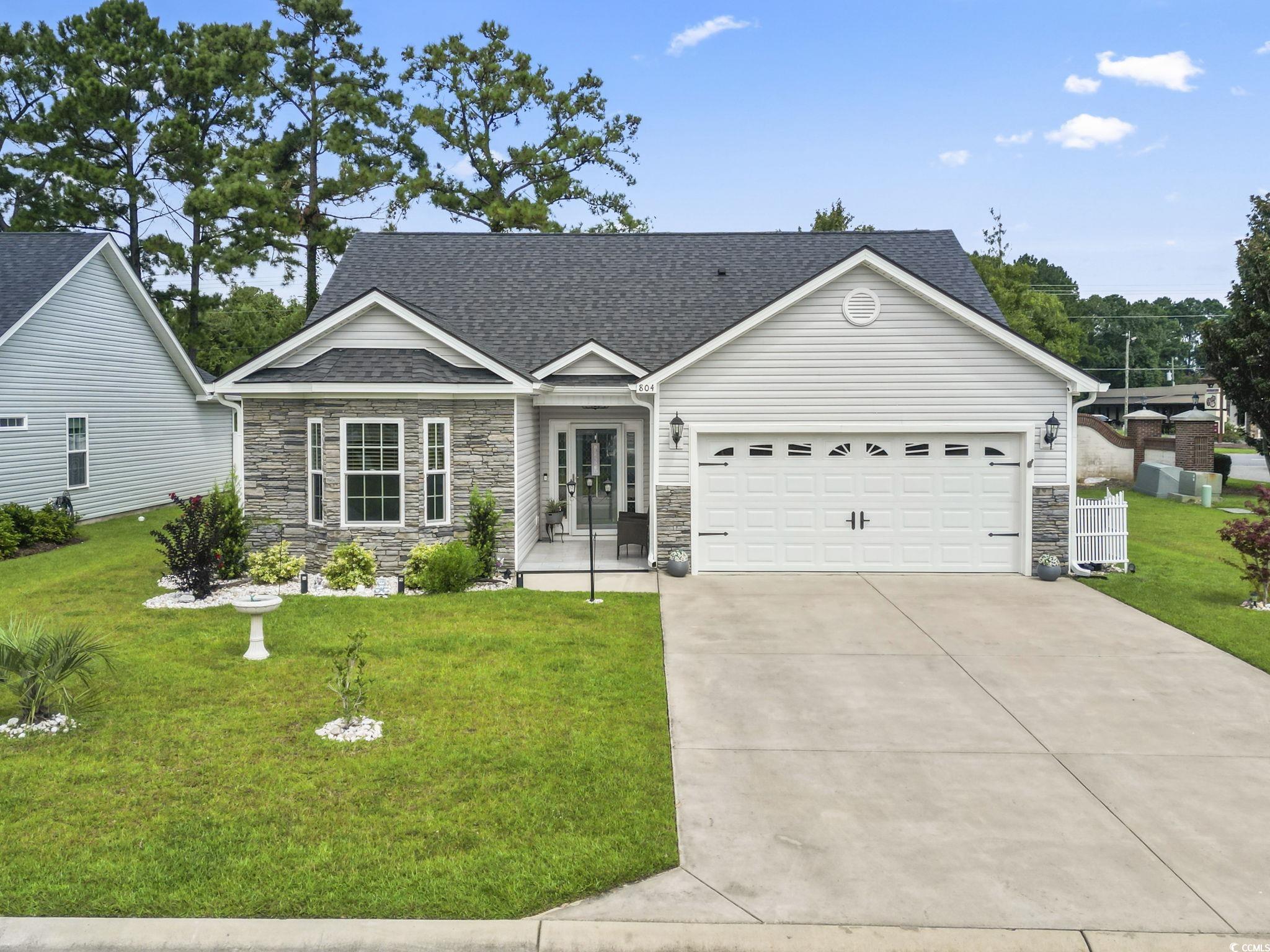 Single story home featuring stone siding, a front yard, an attached garage, roof with shingles, and concrete driveway