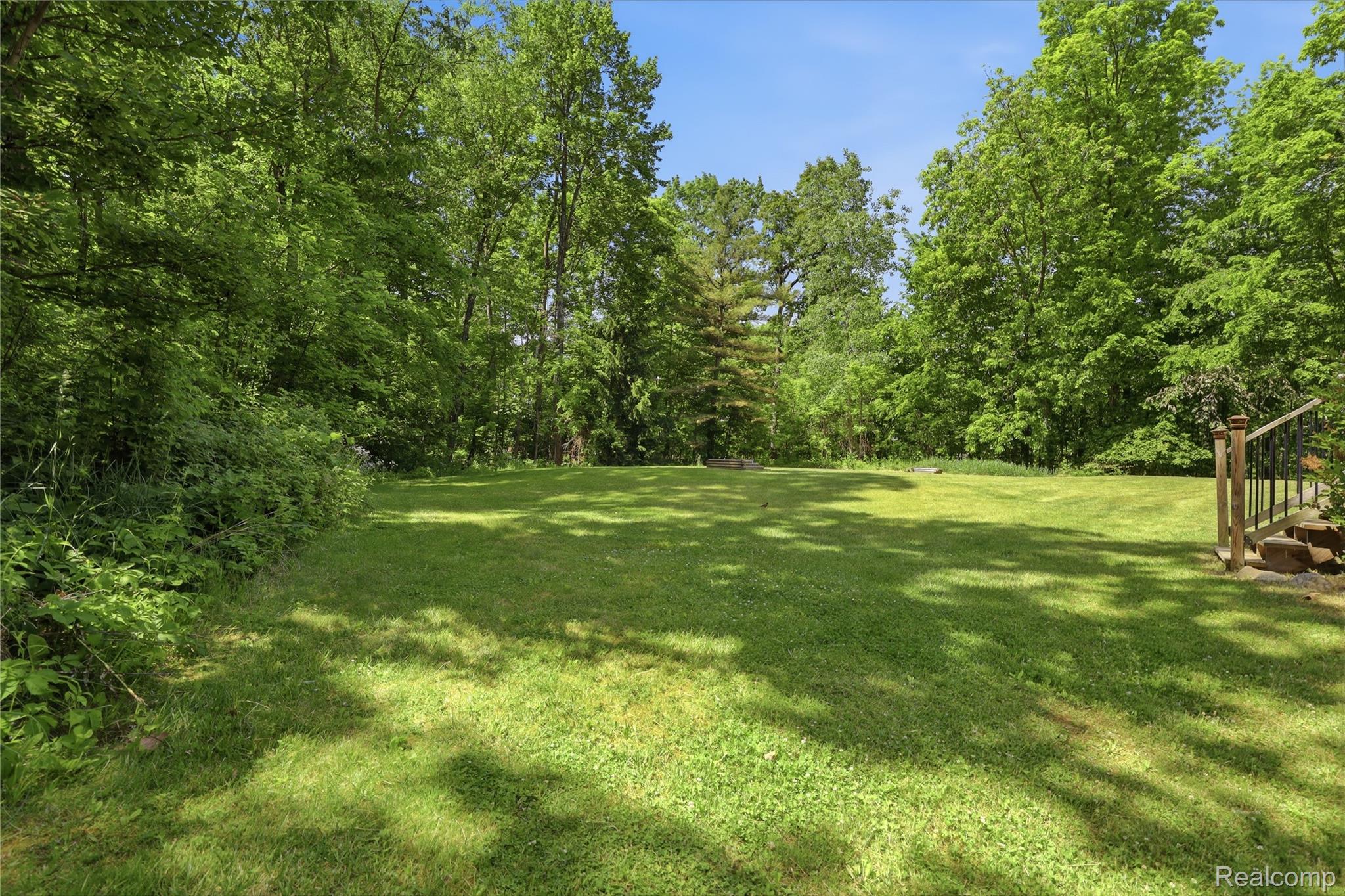 14830 Sheridan Road Byron, MI 48418 - Photo 46 of 74 Expansive green lawn surrounded by mature trees, featuring a wooden deck with railing and stone steps