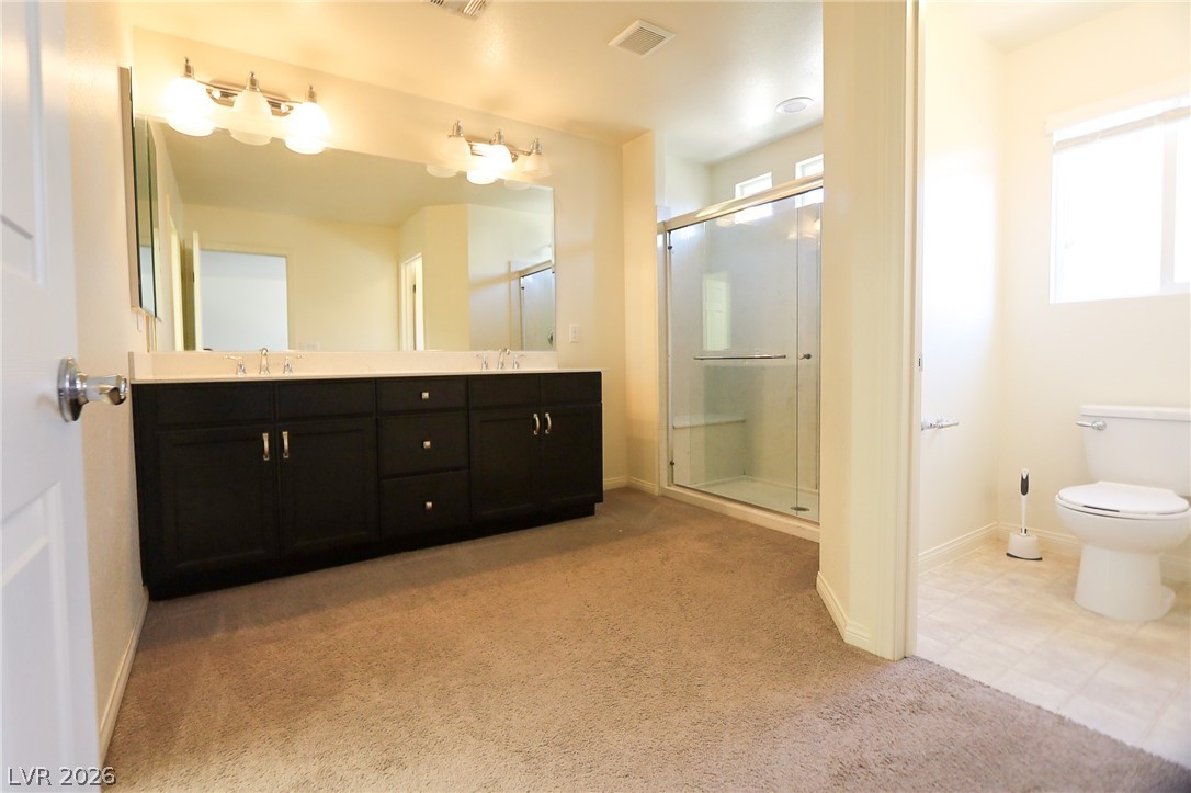 6418 Jackson Spring Road Las Vegas, NV 89118 - Photo 16 of 20 A well-appointed primary bathroom showcases a double vanity, a glass-enclosed shower, and a private toilet area.